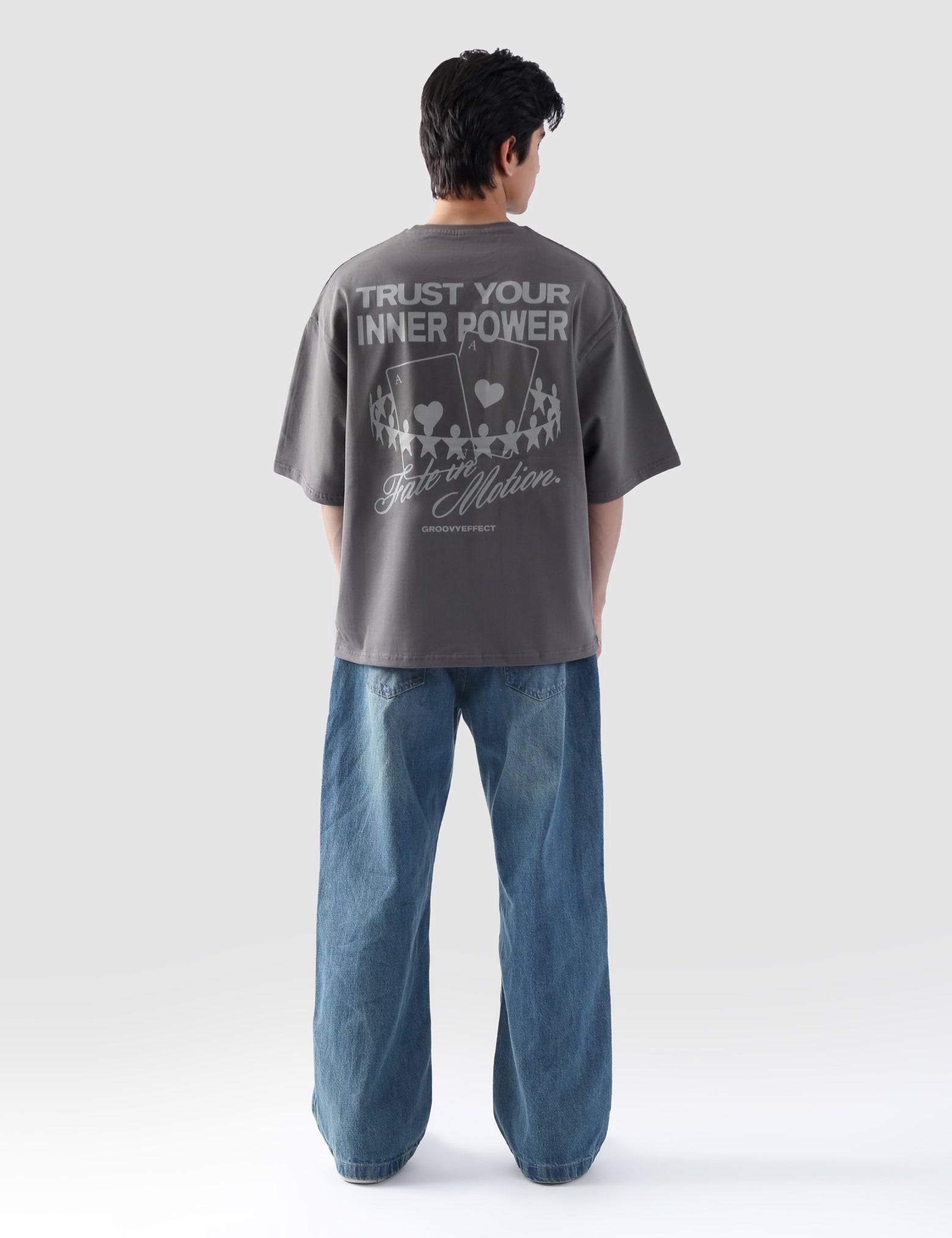 Male model wearing stone grey oversized t-shirt in Pakistan by Groovy – drop shoulder, baggy fit graphic tee styled with loose denim jeans