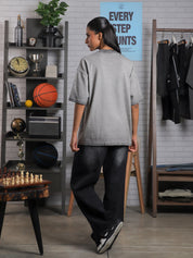 Female model turning away in Cultured Visionaries tee, set in a creative studio with decor including a shelf, basketball, and posters.