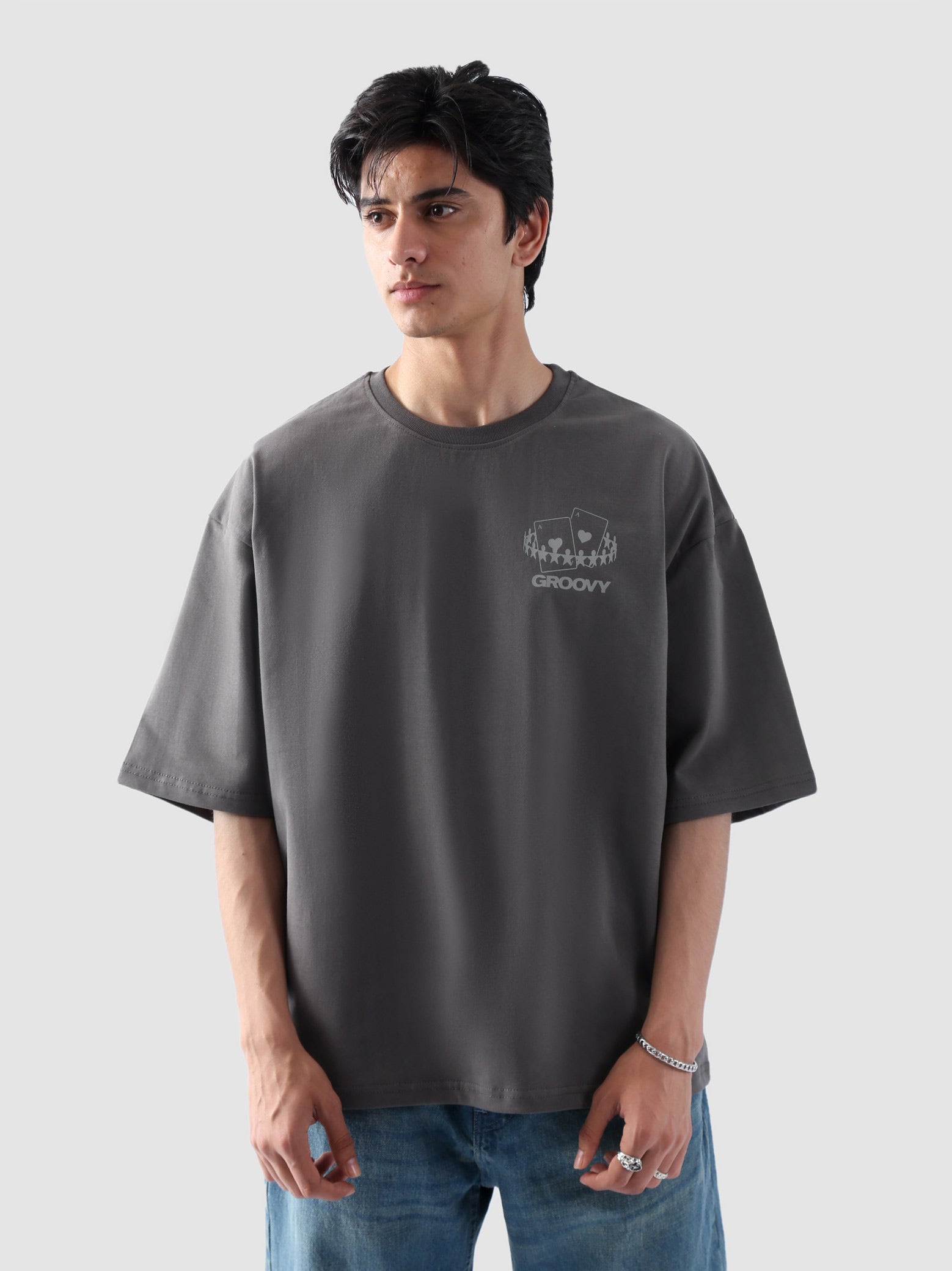 Male model wearing stone grey oversized t-shirt in Pakistan by Groovy – drop shoulder, baggy fit graphic tee styled with loose denim jeans