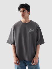 Male model wearing stone grey oversized t-shirt in Pakistan by Groovy – drop shoulder, baggy fit graphic tee styled with loose denim jeans