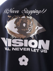 Close-up of the back graphic on the "Never Stopping Culture" t-shirt in navy blue, featuring a bold eye illustration and the text “VISION WILL NEVER LET US” in a mix of puff and screen print, representing unshakeable focus and grind culture.