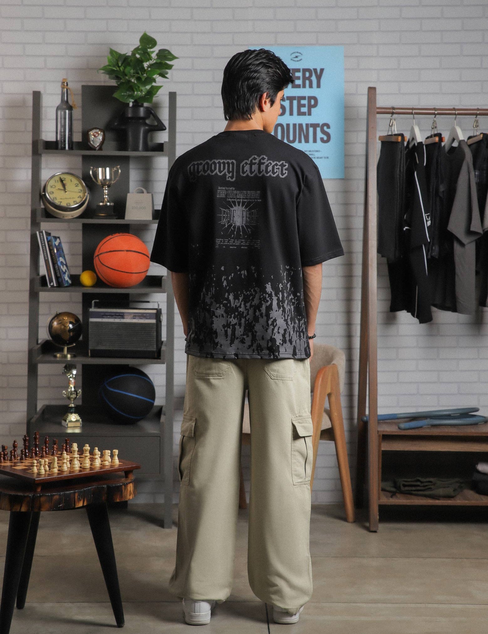Full back shot of black graphic tee with text “Groovy Effect” and “Love Over Fear,” styled by male model in lifestyle backdrop.