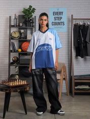 Full body view of woman in oversized blue and white racing jersey and black baggy jeans – Groovy Culture unisex streetwear shot in indoor lifestyle scene Pakistan
