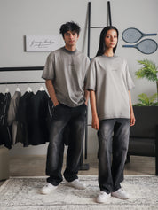 Two models wearing GROOVY Oil Fade Blank t-shirts styled with washed denim, showcasing the gradient oil-dyed texture in a clean indoor studio setup.
