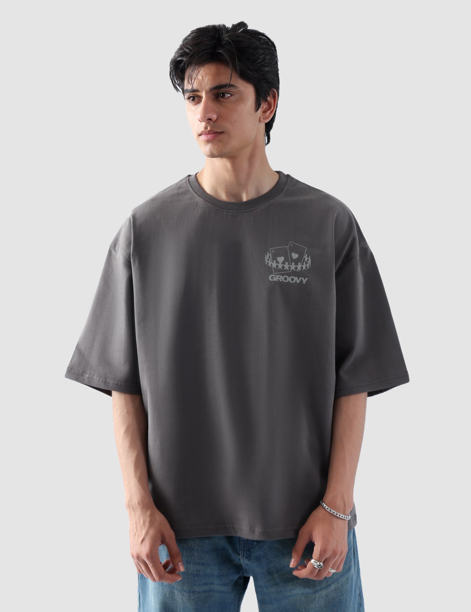 Male model wearing stone grey oversized t-shirt in Pakistan by Groovy – drop shoulder, baggy fit graphic tee styled with loose denim jeans
