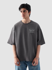 Male model wearing stone grey oversized t-shirt in Pakistan by Groovy – drop shoulder, baggy fit graphic tee styled with loose denim jeans