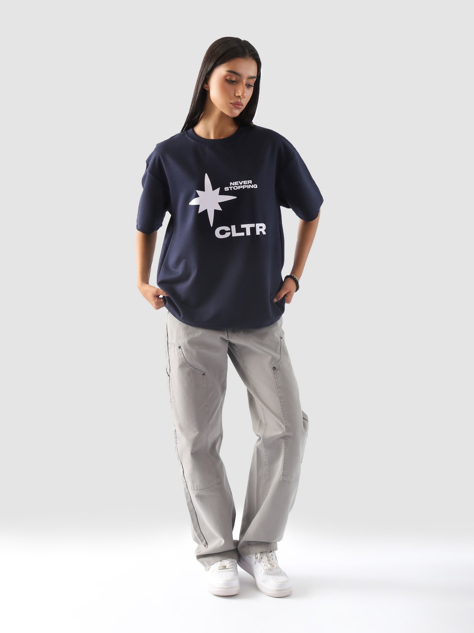 Full-body view of a model wearing the "Never Stopping Culture" tee in navy blue. The oversized fit and front graphic featuring a bold star and "CLTR" text evoke a strong streetwear identity rooted in hustle and ambition.