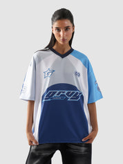 Woman wearing oversized blue and white racing jersey with bold graphics – Groovy Culture unisex streetwear shot in lifestyle indoor setup Pakistan
