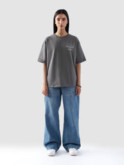 Model wearing stone grey oversized t-shirt for women in Pakistan, styled with wide-leg blue denim jeans— Groovy streetwear graphic tee with relaxed fit and drop shoulder design