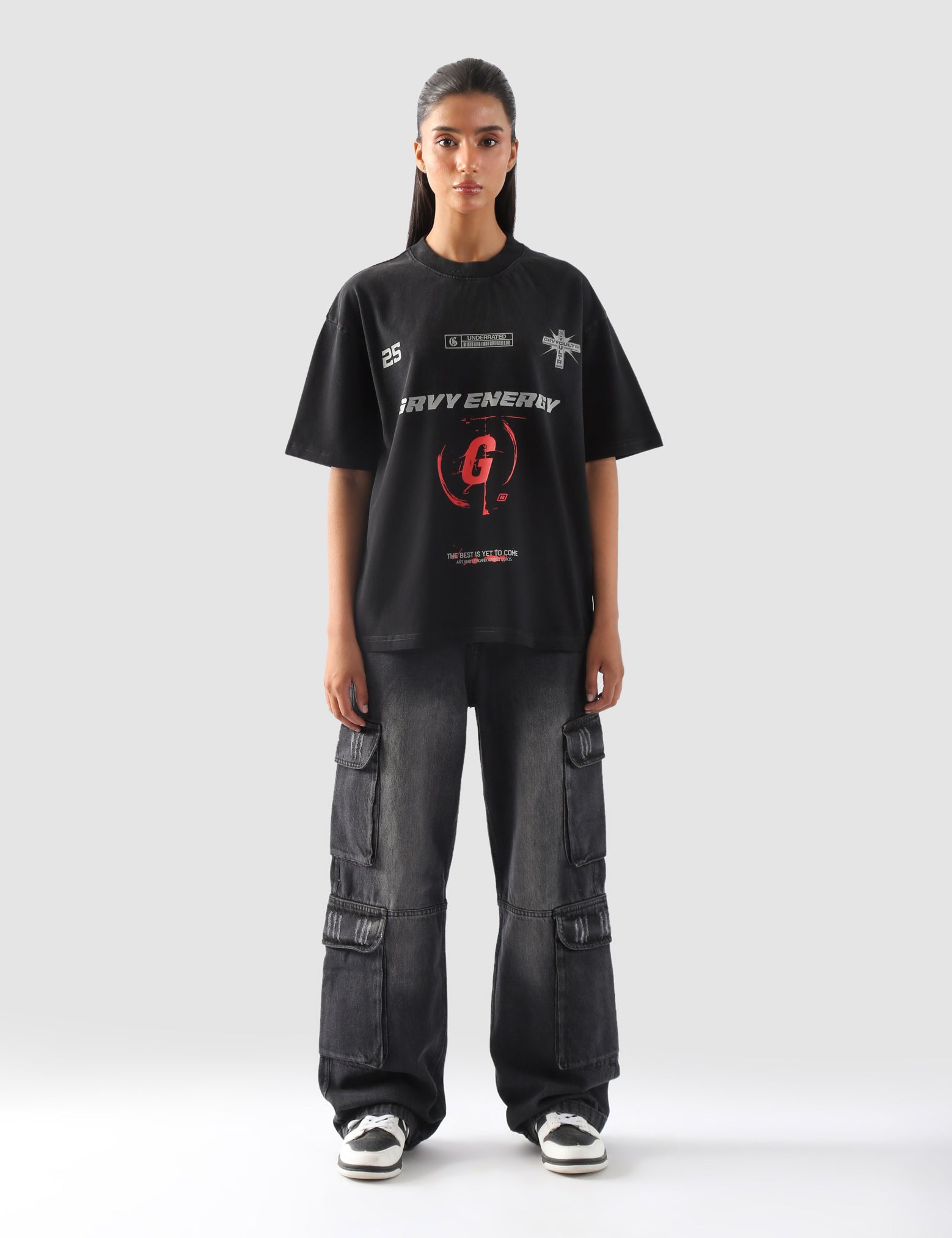 Female model wearing black "GROOVY Energy" oversized streetwear t-shirt with bold red graphics and wide-leg cargo jeans – front full view.