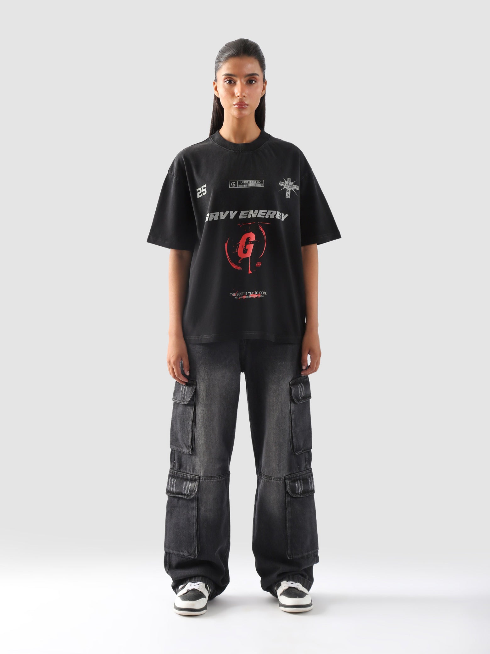 Female model wearing black "GROOVY Energy" oversized streetwear t-shirt with bold red graphics and wide-leg cargo jeans – front full view.