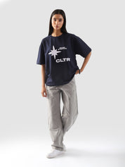 Full-body view of a model wearing the "Never Stopping Culture" tee in navy blue. The oversized fit and front graphic featuring a bold star and "CLTR" text evoke a strong streetwear identity rooted in hustle and ambition.