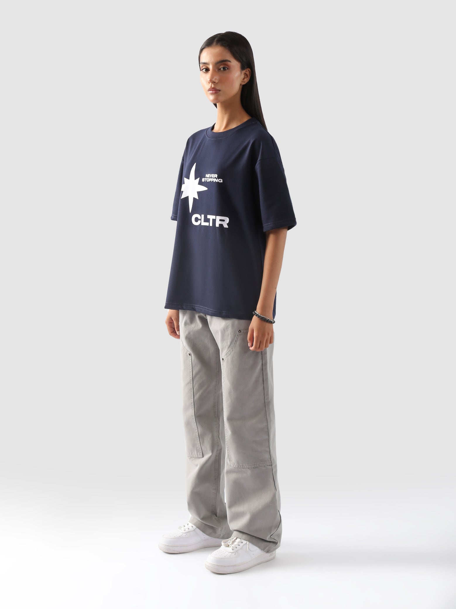 side-body view of a model wearing the "Never Stopping Culture" tee in navy blue. The oversized fit and front graphic featuring a bold star and "CLTR" text evoke a strong streetwear identity rooted in hustle and ambition.
