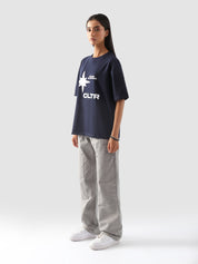 side-body view of a model wearing the "Never Stopping Culture" tee in navy blue. The oversized fit and front graphic featuring a bold star and "CLTR" text evoke a strong streetwear identity rooted in hustle and ambition.