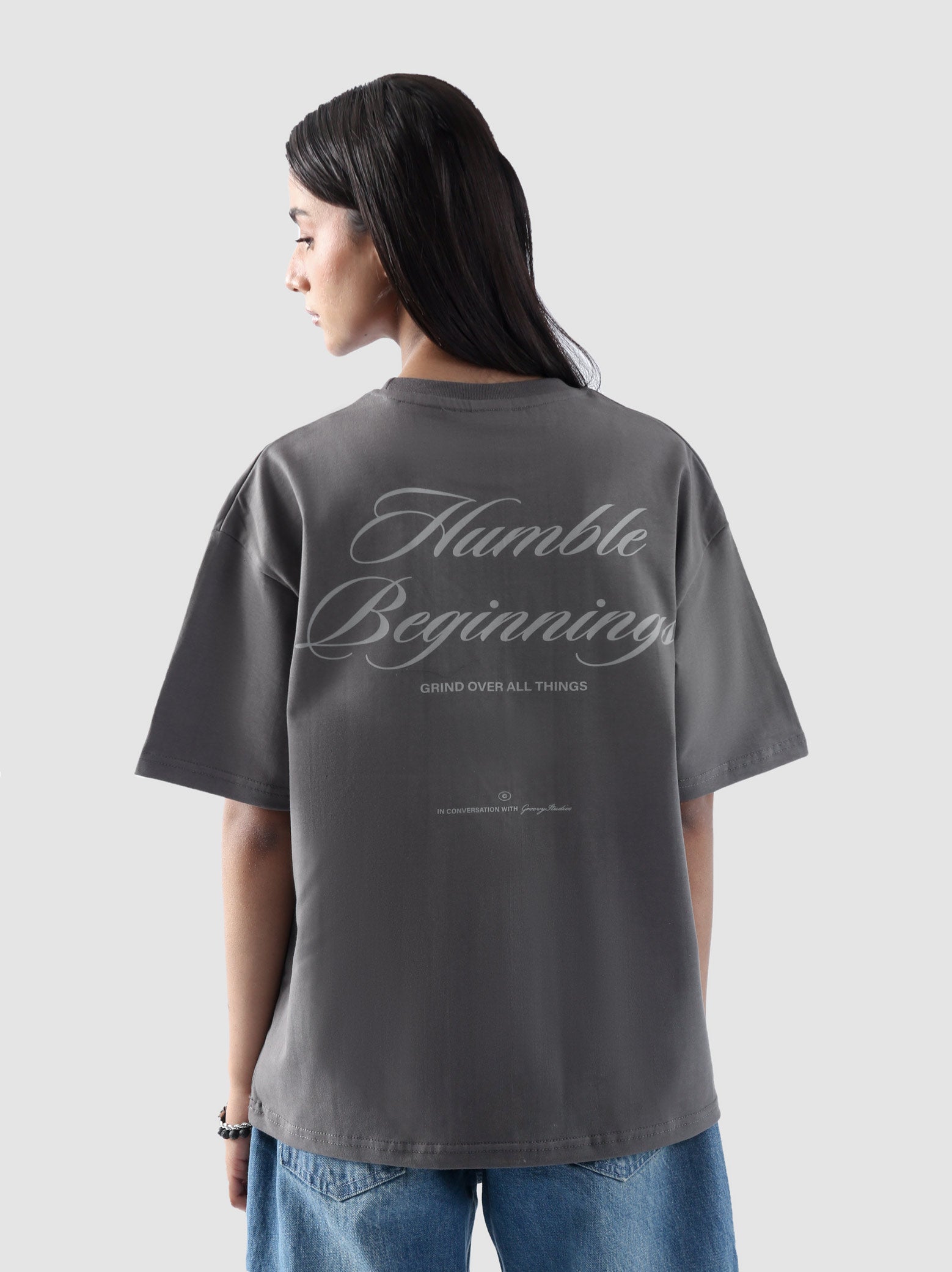 Back view of woman wearing grey oversized t-shirt with 'Humble Beginnings' graphic – unisex streetwear by Groovy Pakistan
