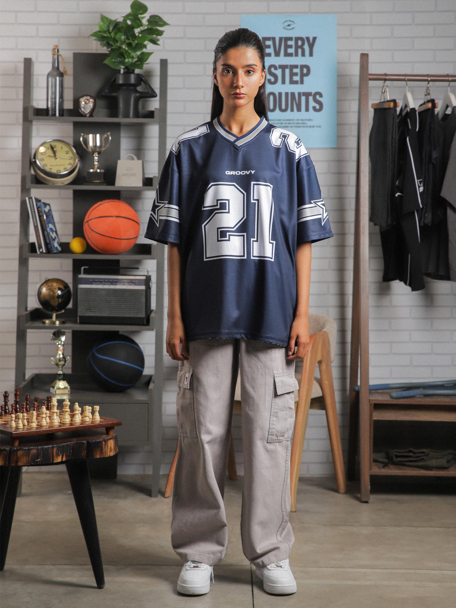 Front view of female model wearing GROOVY All Stars Basketball Jersey in navy blue, standing in a lifestyle setup with basketball and chess props.