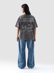 Model wearing stone grey oversized t-shirt for women in Pakistan, styled with wide-leg blue denim jeans – Groovy streetwear graphic tee with relaxed fit and drop shoulder design