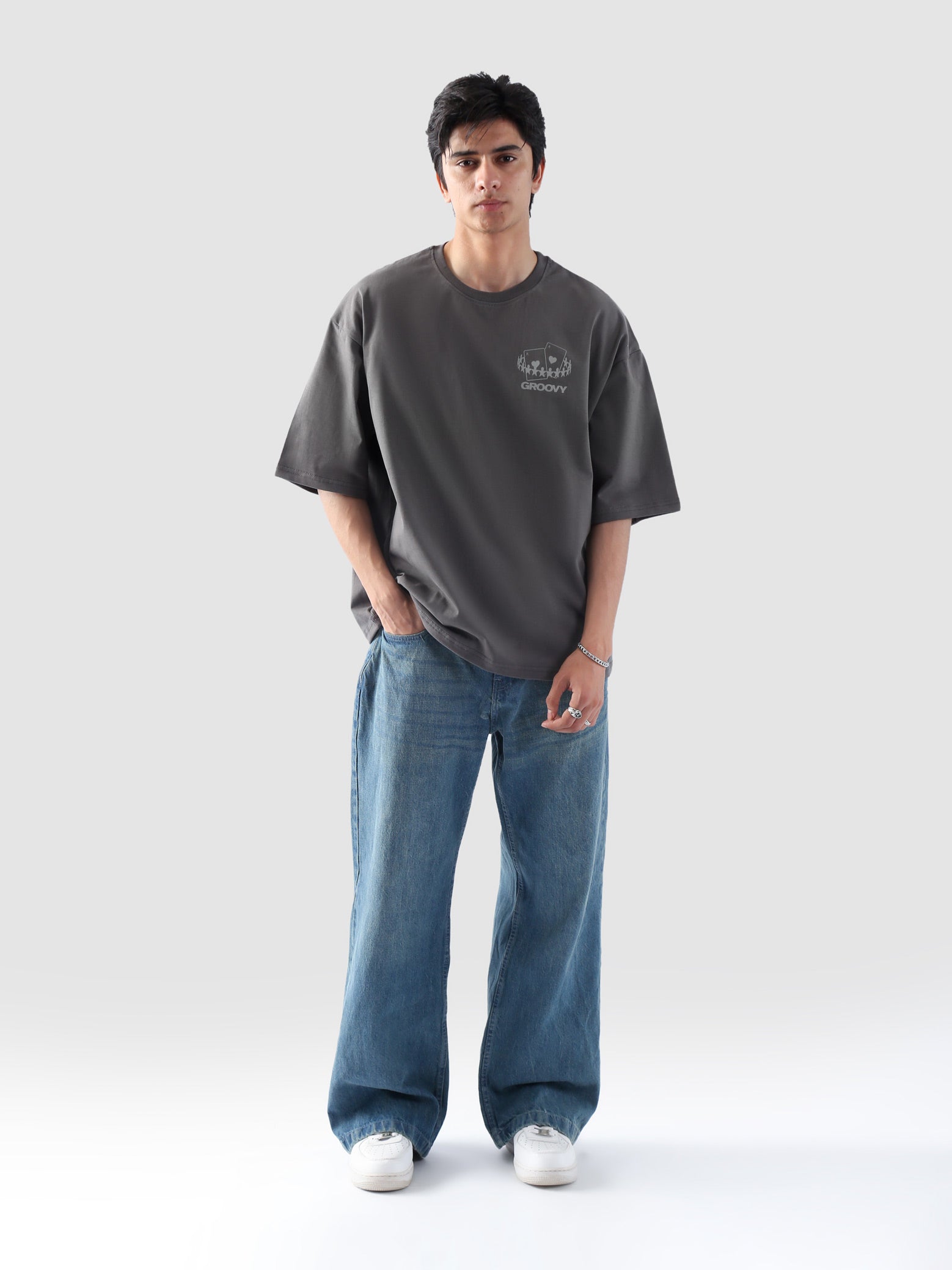 Male model wearing stone grey oversized t-shirt in Pakistan by Groovy – drop shoulder, baggy fit graphic tee styled with loose denim jeans