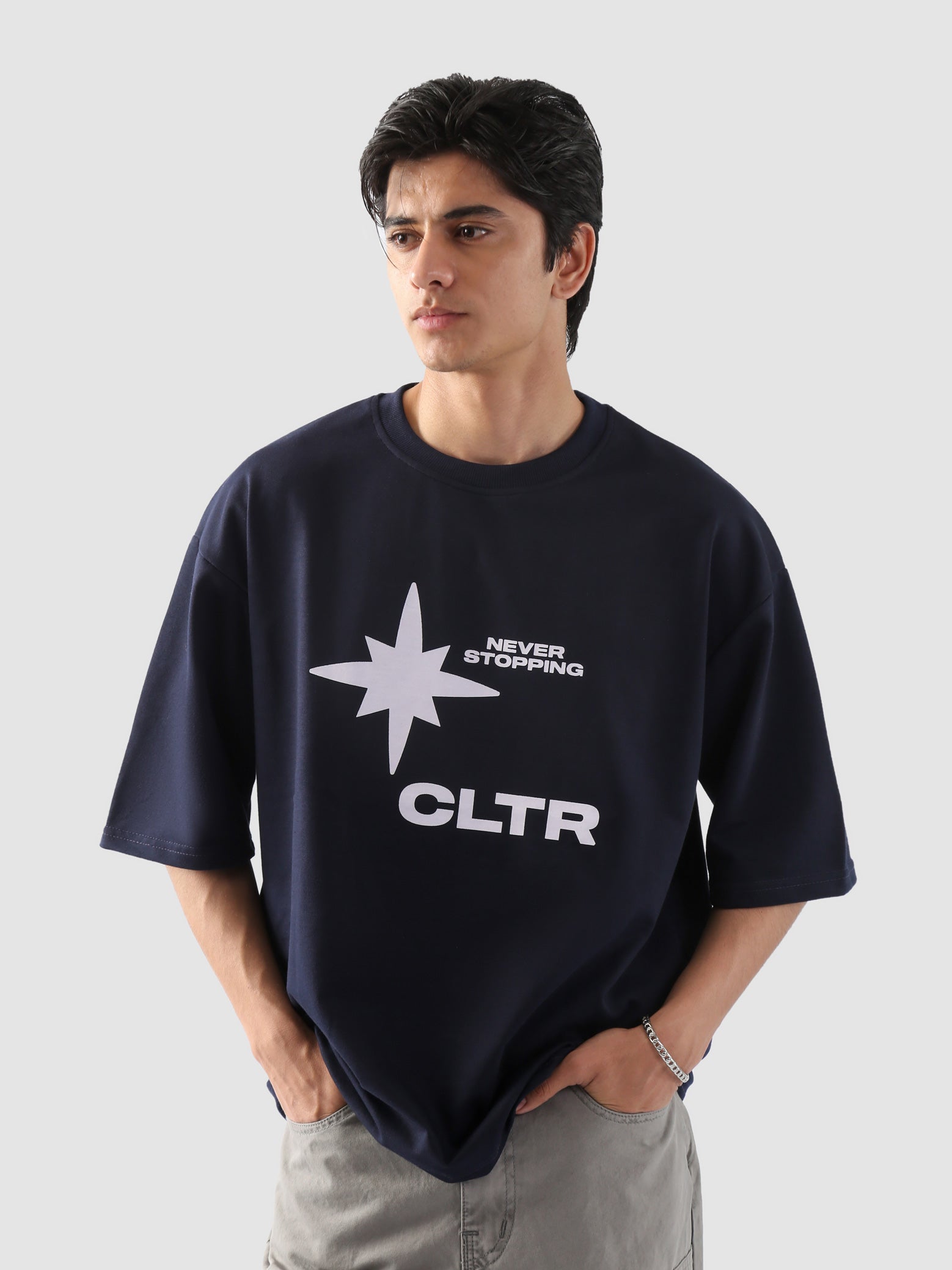 Close-up of a male model wearing the "Never Stopping Culture" oversized navy blue t-shirt, featuring a bold white star graphic with the text “NEVER STOPPING CLTR,” styled with light grey cargo pants and hands tucked in pockets.