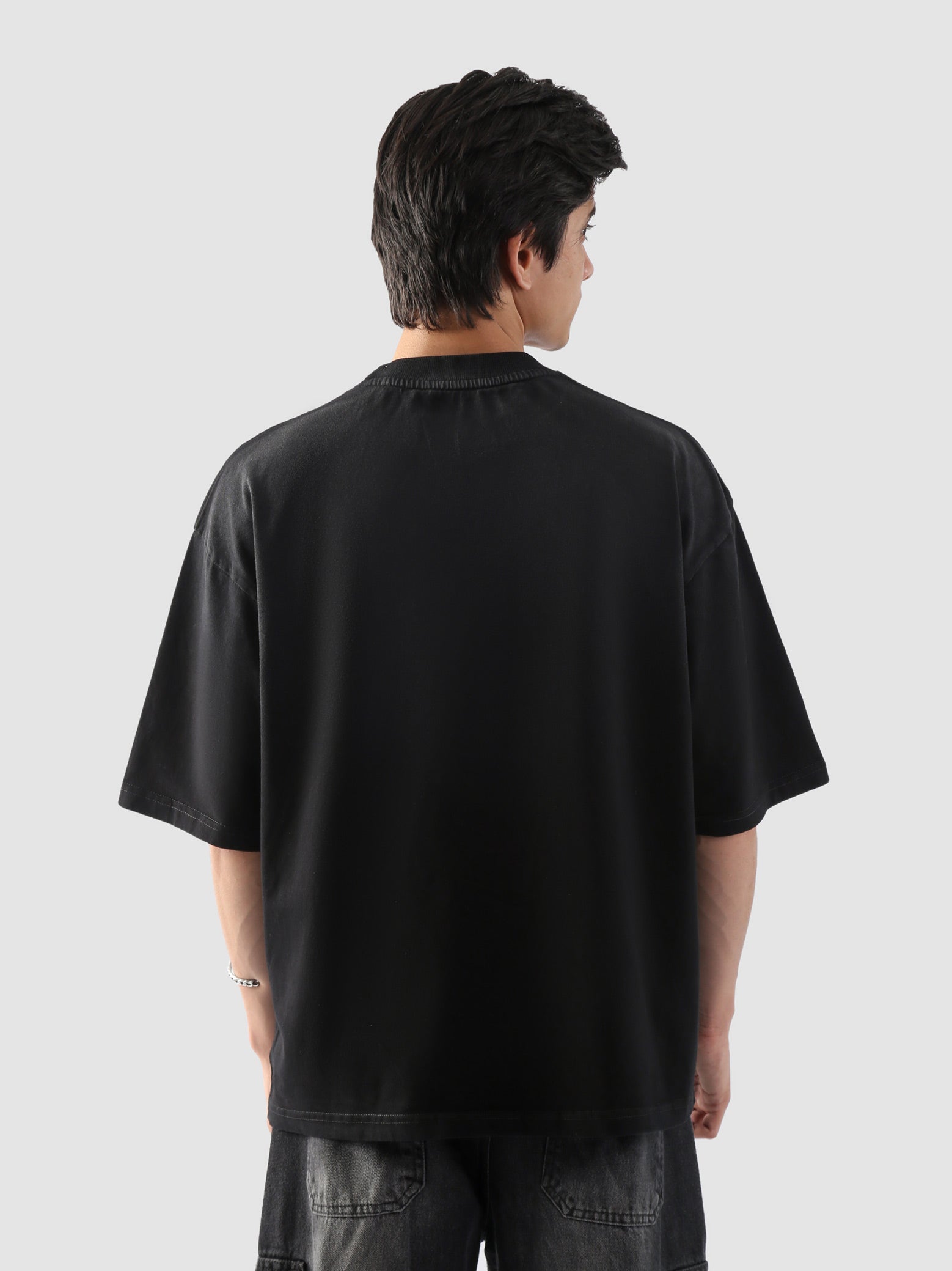 Rear view of black t-shirt worn by male model – minimal back with emphasis on oversized cut and street-style fit.