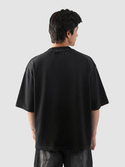 Rear view of black t-shirt worn by male model – minimal back with emphasis on oversized cut and street-style fit.